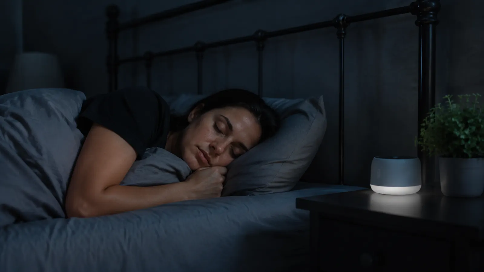 Person sleeping soundly in a dark bedroom with a sound machine running on the nightstand